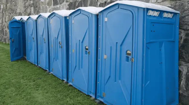 Row of blue portable toilets lined up on grass against a stone wall for event sanitation in Fort Collins, CO