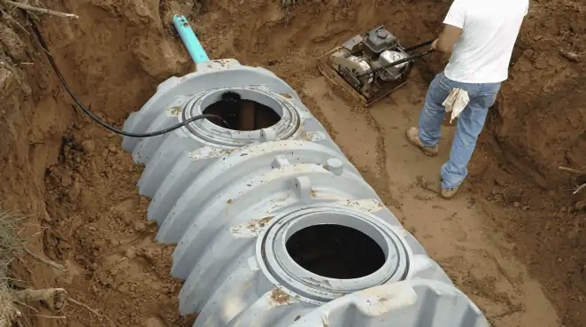 Septic tank installation showing a technician compacting soil around a new poly septic tank in an excavation pit in Fort Collins, CO